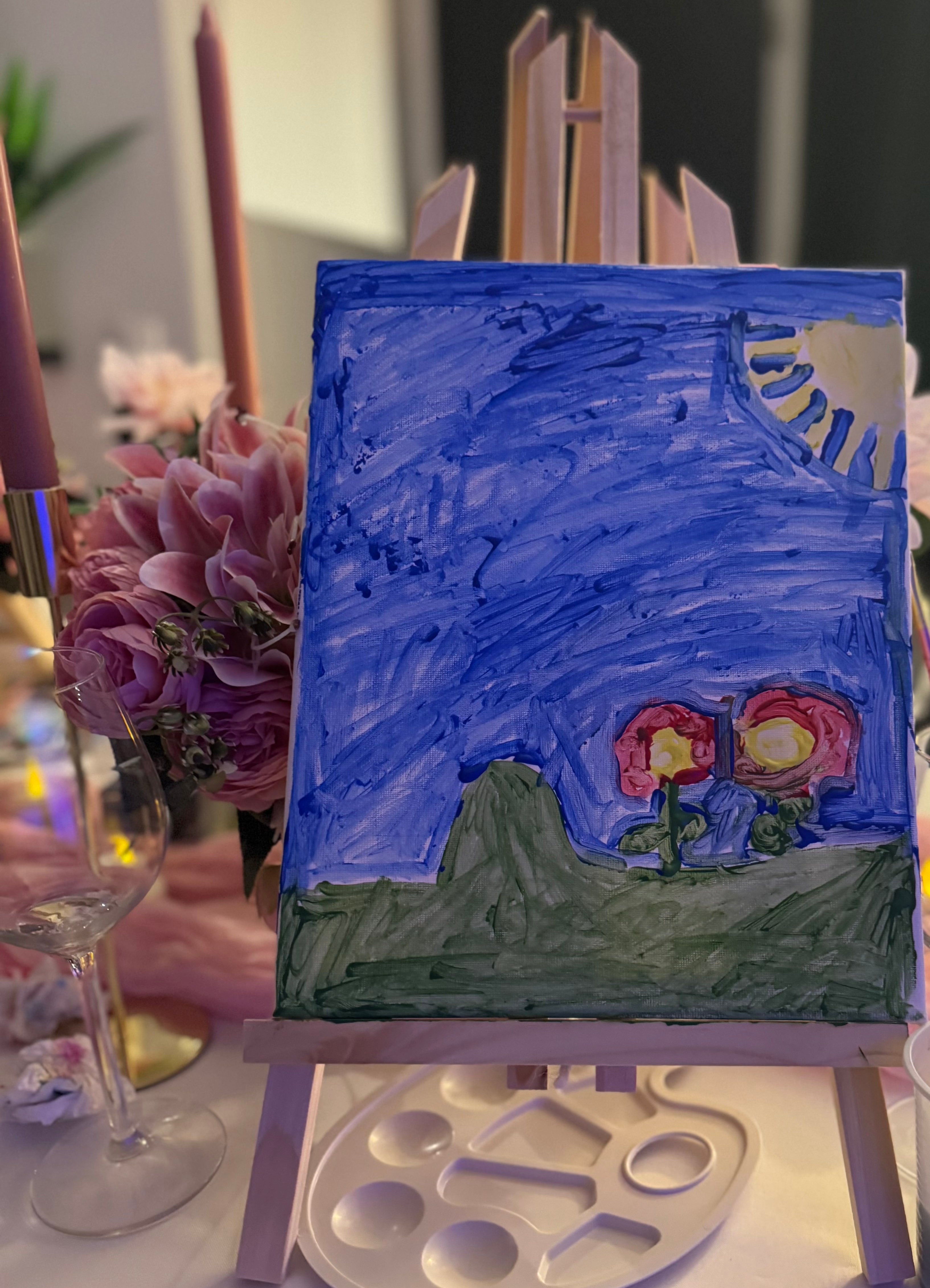 Petite toile sur chevalet représentant un paysage de nuit bleu avec colline verte et deux fleurs rouges.