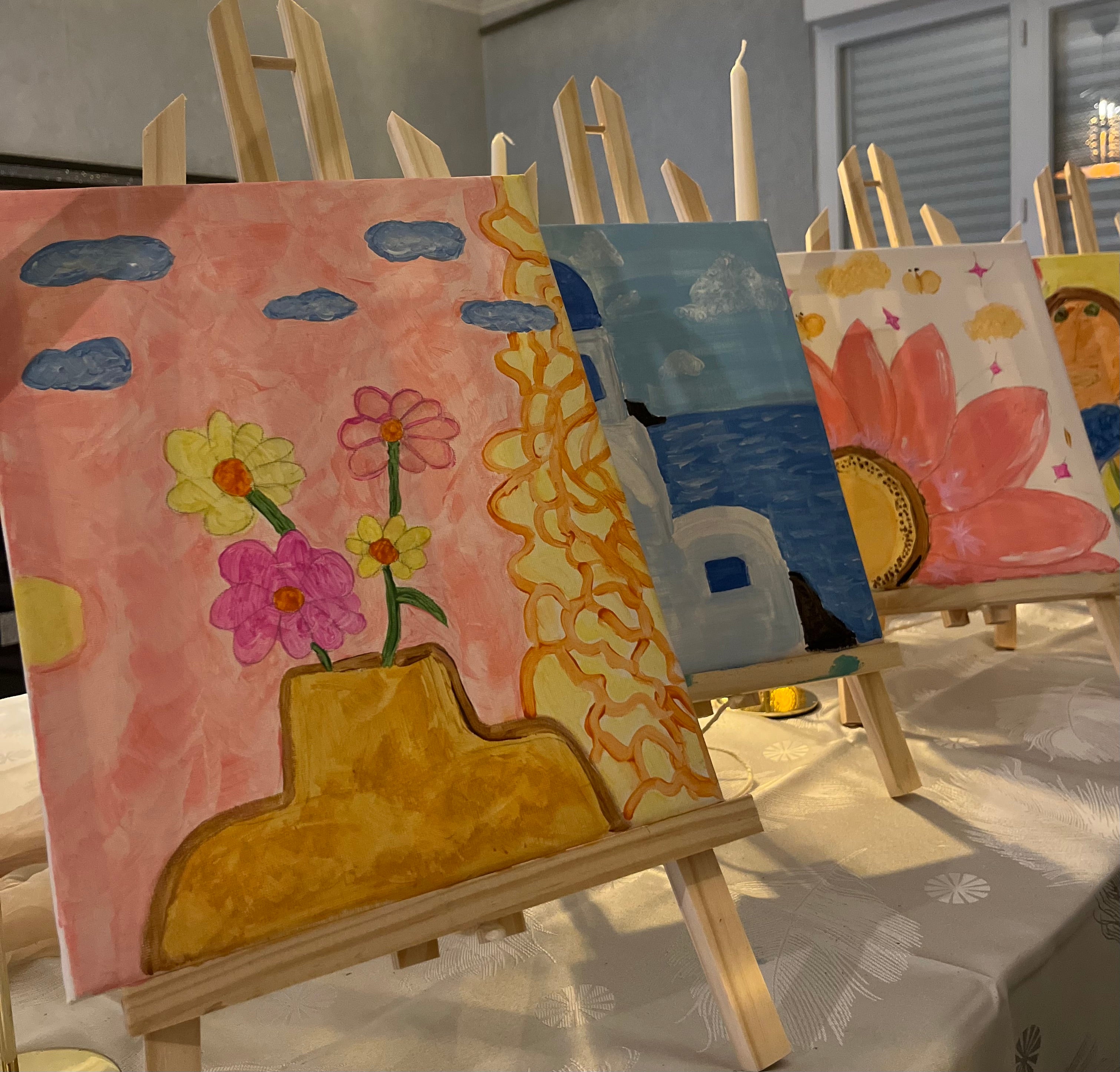 Toile pastel avec colline ocre, maison blanche et fleurs roses sur une table de soirée App’art.