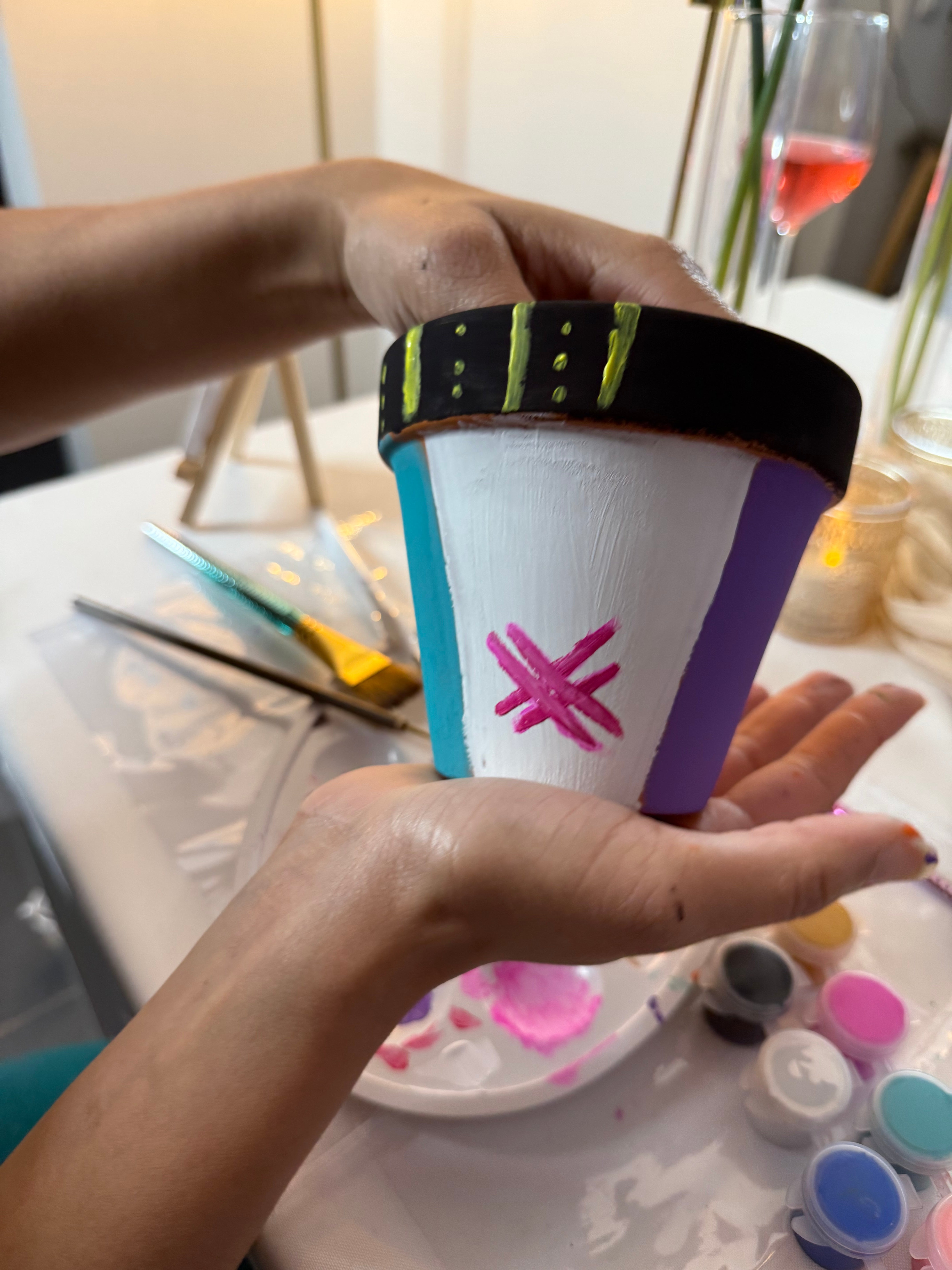 Pot en terre cuite peint à la main, blanc avec bord décoré et motif étoile violette, tenu dans une main.